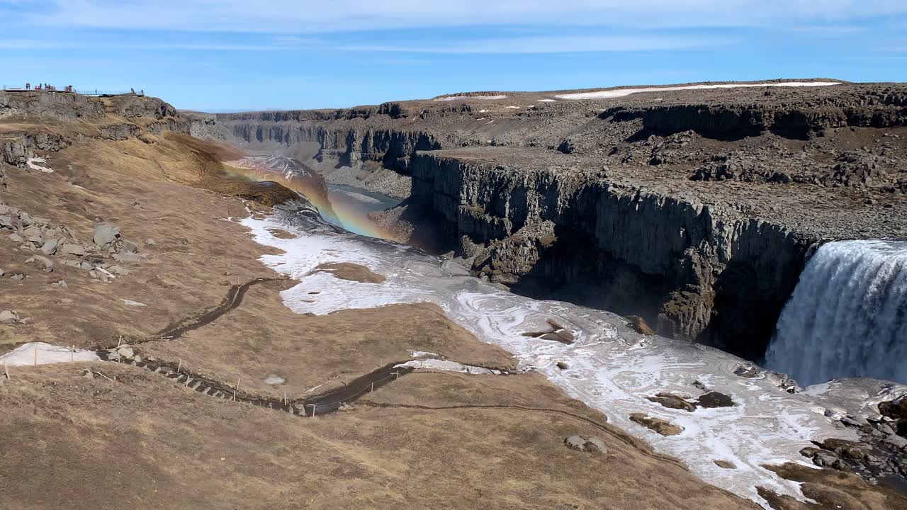 Det tørre og steinete islandske landskapet rundt Dettifoss, som er en av Europas mektigste fossefall, på en solrik dag med en vakker regnbue som dukker opp på himmelen