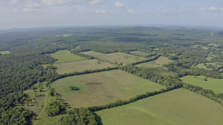 4K aerial high over green fields surrounded by woodland with hills in distance