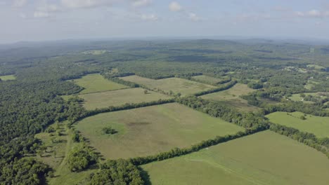 4K-Antenne-Hoch-über-Grünen-Feldern,-Umgeben-Von-Wäldern-Mit-Hügeln-In-Der-Ferne