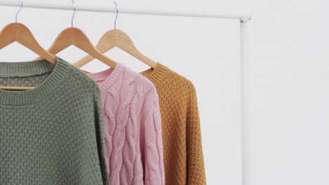 Video-of-three-multi-coloured-sweaters-on-hangers-and-copy-space-on-white-background