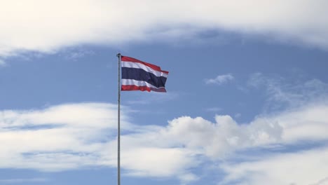 waving the kingdom of thailand flag on a pole with blue sky and white clouds in the background