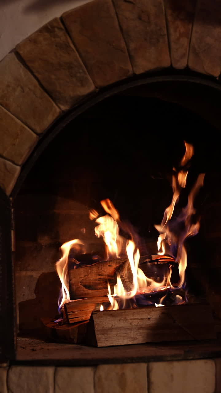 Beautiful stone fireplace. Wood burning in a fireplace. Warm cozy fire in a fireplace during winter holidays. Home cosiness. Vertical video