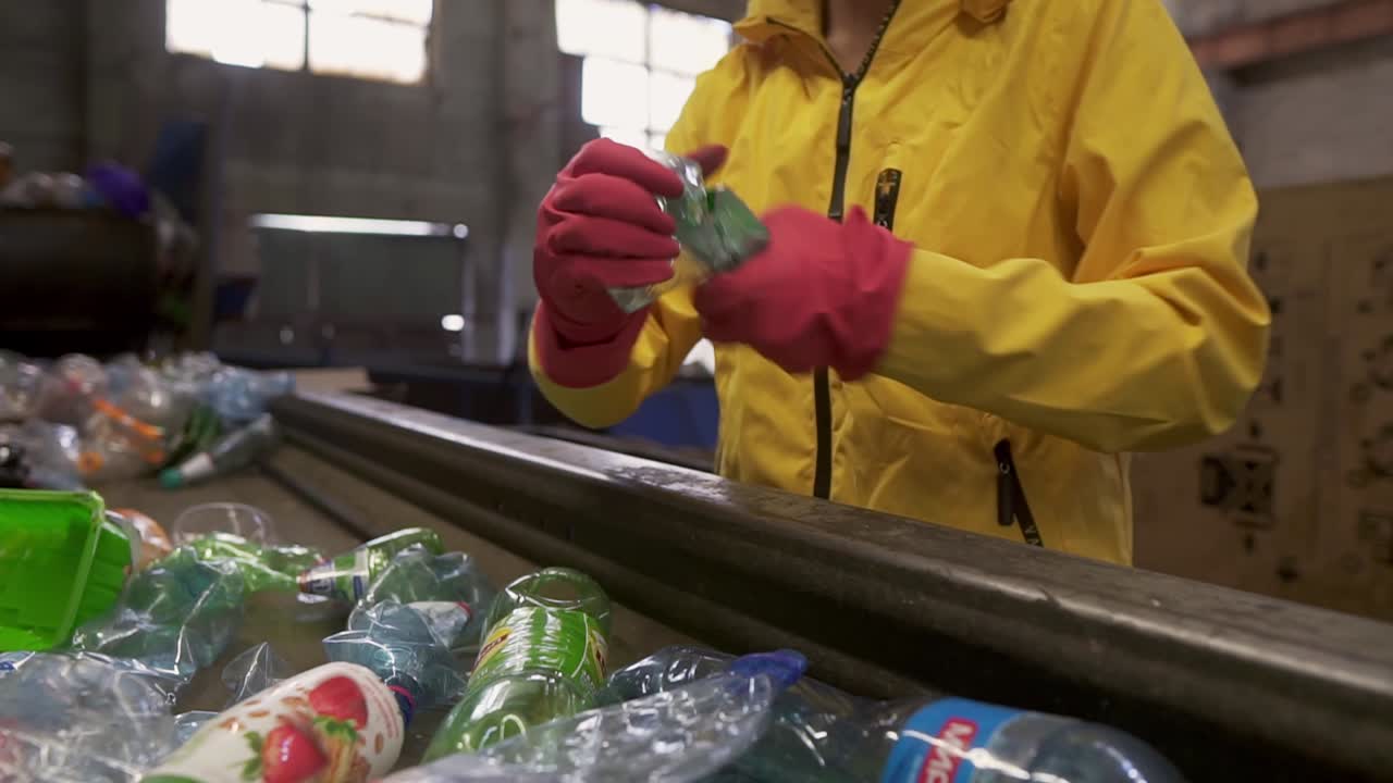 persona irreconocible con chaqueta amarilla y guantes clasificando botellas de plástico usadas en la planta de reciclaje. separar las botellas en la línea, exprimirlas y ponerlas en la caja