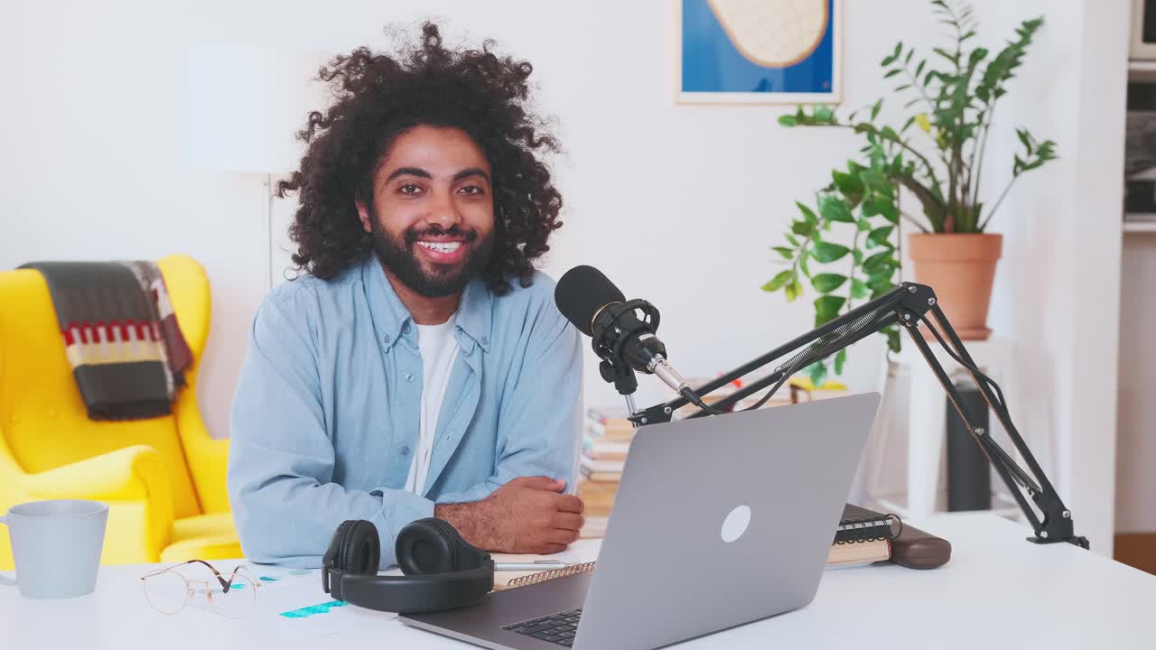 Pria Arab muda melepas headphone dan melihat ke kamera, duduk di meja kantor.