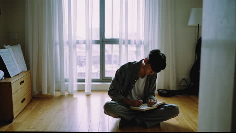 young man writing in notebook at home