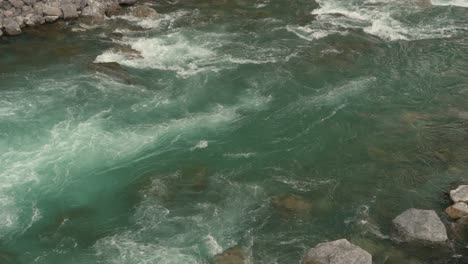 panning down a clear blue river full of water as it streams down among rocks along the riverbank