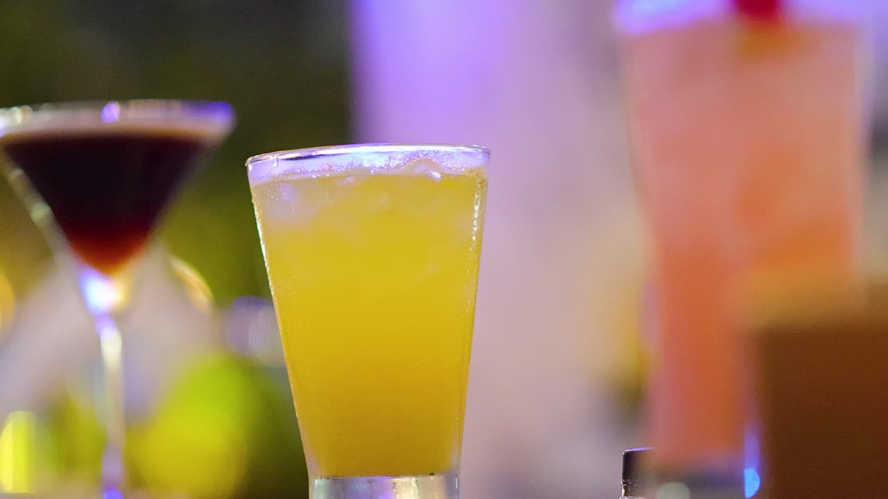 Vibrant cocktails on bar table, colorful lighting, shallow depth of field, smooth camera pan, nighttime