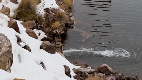 Large-Valve-filling-a-pond-with-snow-around-bank,-fast-flowing-water