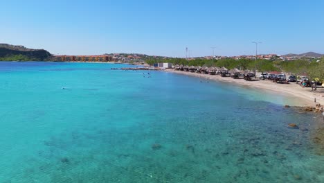 pristine shoreline at caracasbaai beach, curacao, turquoise waters and lush coastal vegetation under a clear sky with tropical picnic tables on sand
