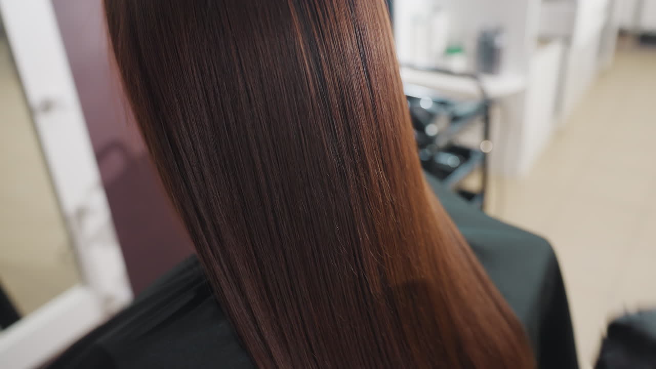 post treatment caucasian woman with glossy long brown hair, stylist in gloves combing sleek ends, bright salon lighting highlighting silky texture and healthy shine, professional conditioning