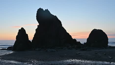 towering sea stacks cast dramatic shadows on the beach at twilight with a colorful sky behind