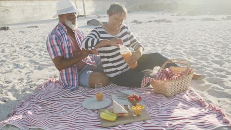 una feliz pareja afroamericana senior haciendo picnic en la playa, cámara lenta.