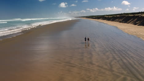 aerial view of a young couple walk hand in hand along the ninety mile beach, new zealand