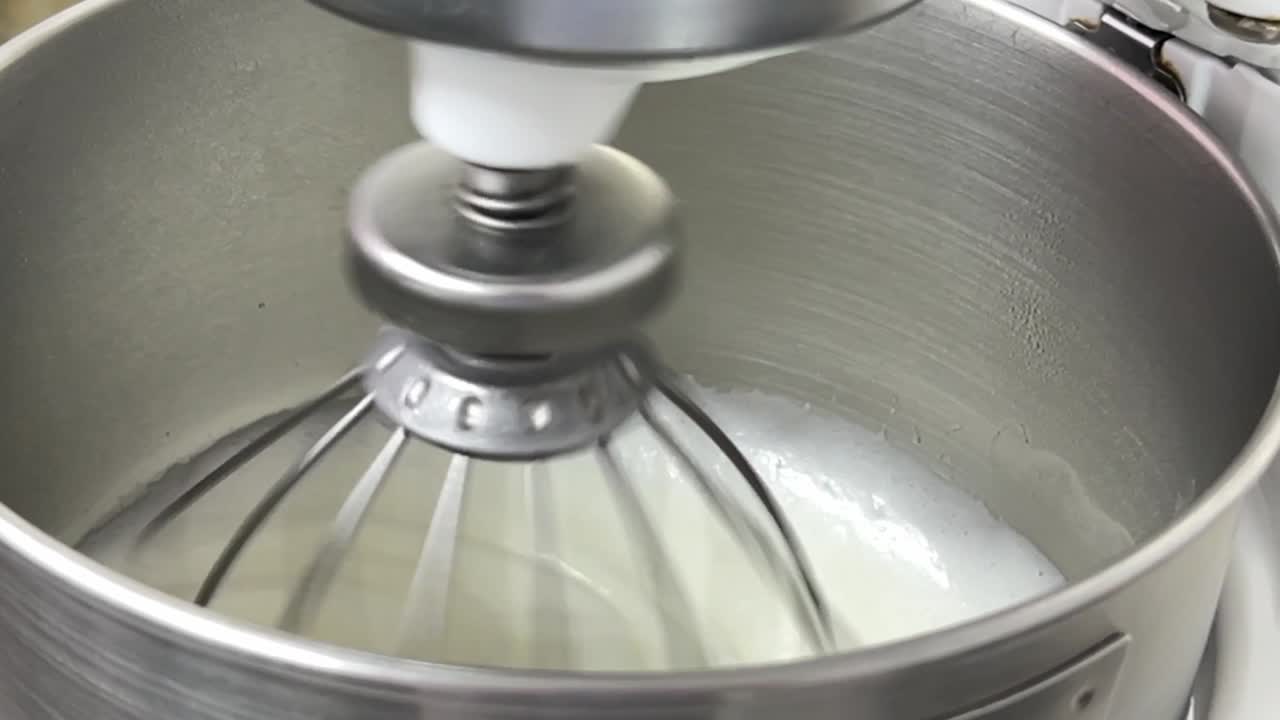 Slow motion delicious icing meringue buttercream mixing in the heavy duty mixer in the commercial bakery setting, close up shot