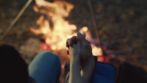 couple holding hands by a campfire