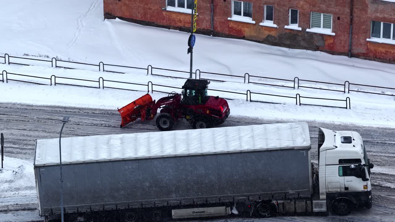 Sneplov rydder vej ved siden af en lastbil på en snefyldt dag i vinterbyen.