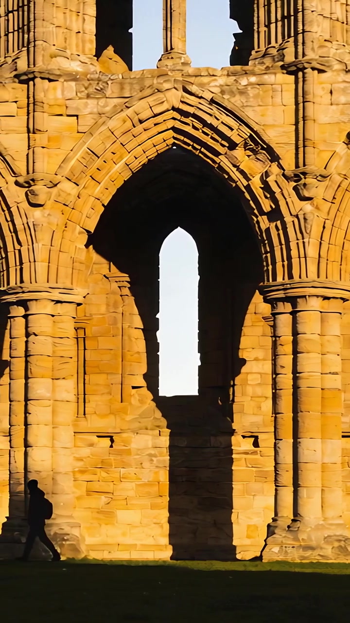 Video verticale: Persona con zaino che cammina, illuminata dal sole, che si muove a sinistra oltre archi di pietra, con spazio per il testo.
