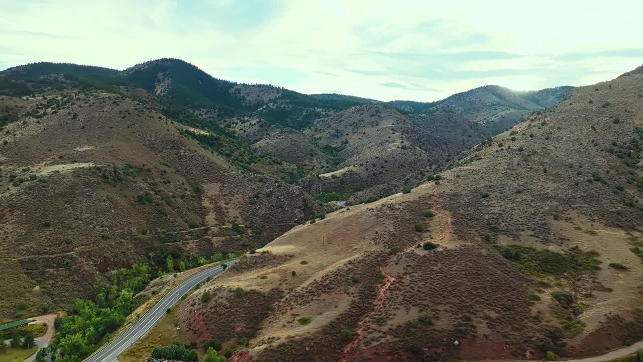 Drone pans across foothills near Red Rocks Amphitheatre Colorado showing layered terrain and rocky desert backdrop, establish
