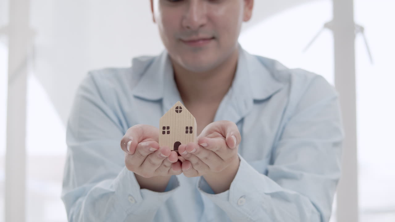 un hombre sostiene un modelo de casa pequeña que simboliza las aspiraciones de ser propietario de una casa en un estudio luminoso y aireado.