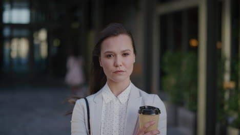 portrait young confident business woman looking serious corporate professional holding coffee wind blowing hair in urban outdoors background ambition success