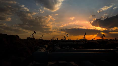 pipeline and working oil pump jacks in a against sunset extracting crude oil. pumping fossil oil is one of the methods of energy generation from renewable energy sources