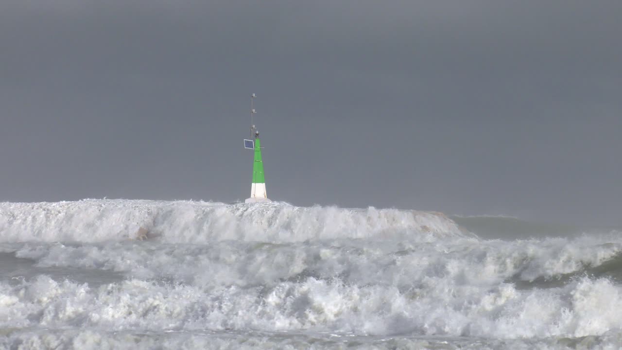 Harbor entrance in stormy seas, waves breaking over sea wall, slow motion
