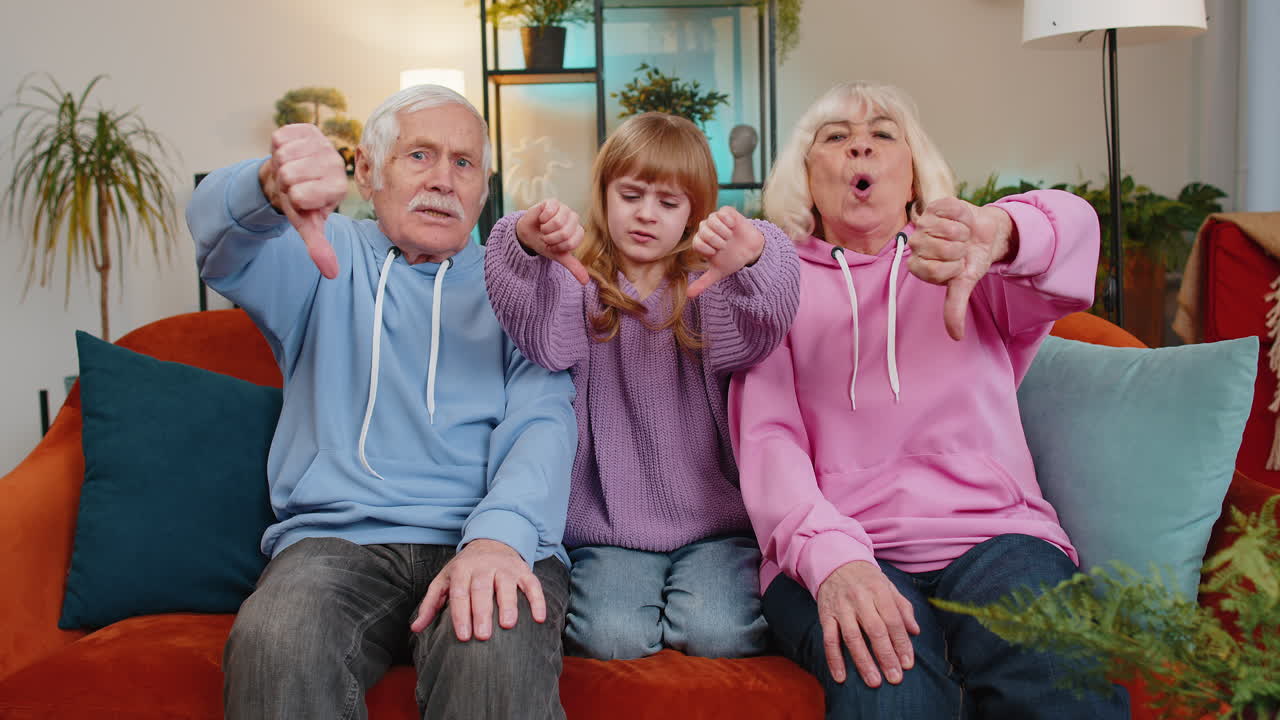 Child girl kid granddaughter with grandparents showing thumbs down disapproval dissatisfied dislike