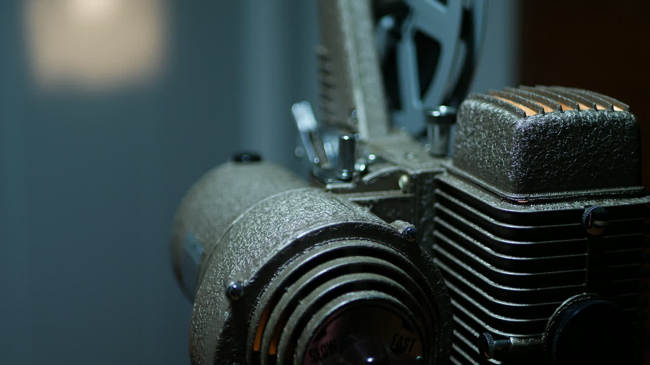 Close up on an old 8mm projector as it projects a movie in the background, the reel is spinning, and it has a shallow depth of field.