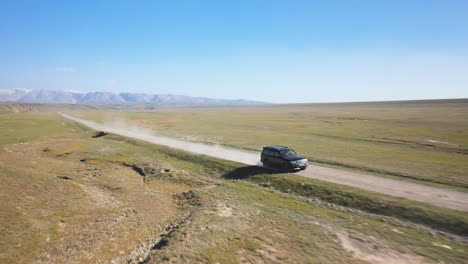 slow rotating cinematic drone shot of an suv going down the road near the kel-suu lake in kyrgyzstan