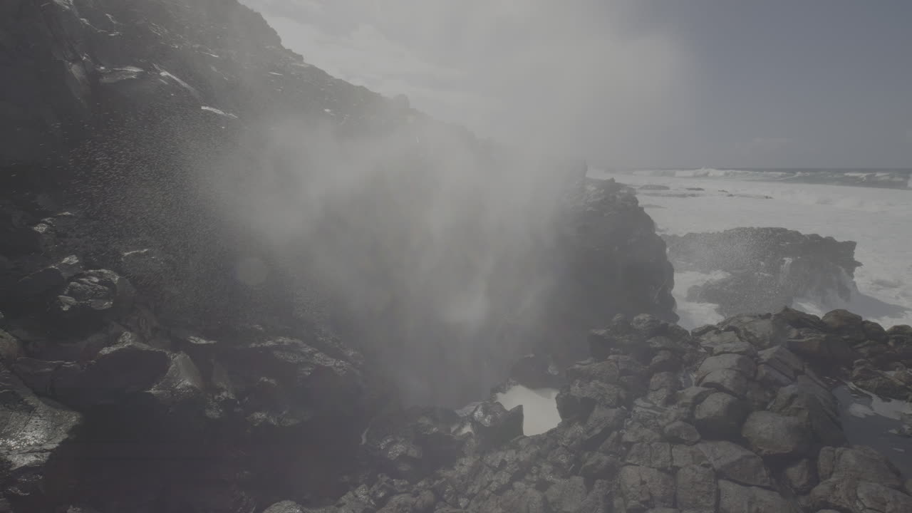 Powerful ocean waves crashing against volcanic rocks, creating a blowhole