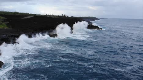 Fly-over-and-into-volcanic-cliffs-with-waves-hitting-cliffs-and-vegetation-behind