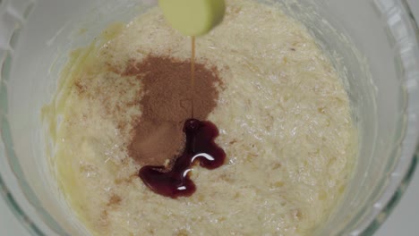 pouring teaspoon of vanilla extract into yellow batter, slowmo overhead closeup