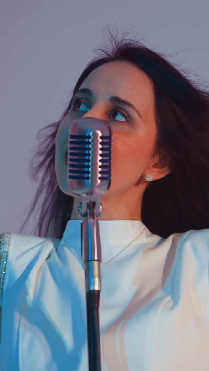 색 드레스를 입고 손을 높이 들고 미소 짓는 가수, 몸이 표현적으로 움직이며 빈티지 마이크로 연주합니다. 분홍색과 파란색의 배경에 설정