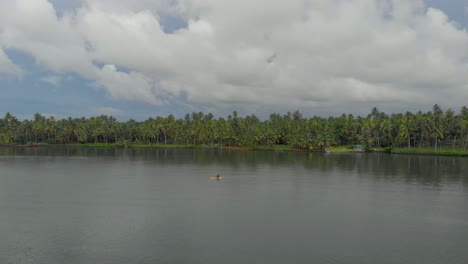 4k aerial drone shot of a 28-year-old indian male paddling a kayak with safety gears in the backwaters of varkala surrounded by coconut tress, kerala