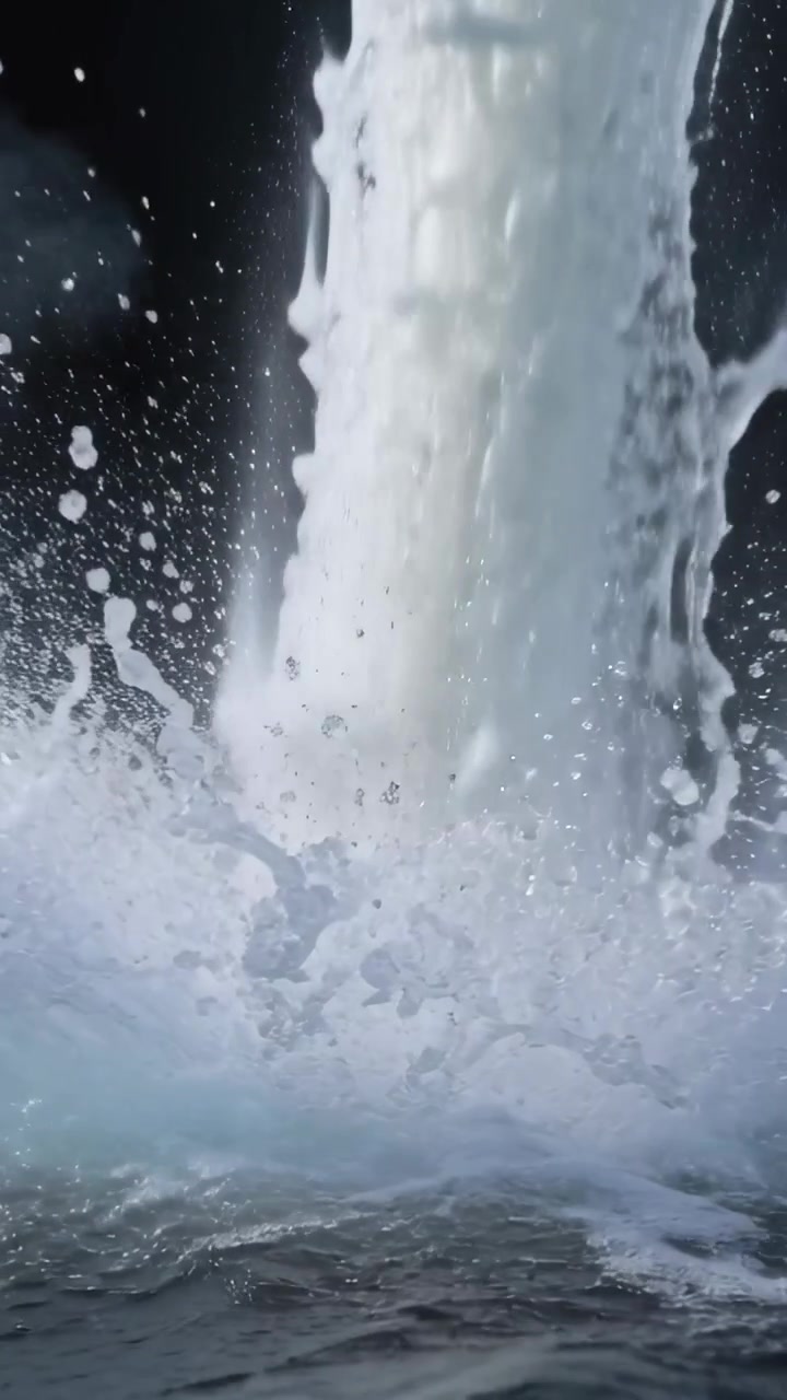 Video vertical: Columna de agua vertical cayendo sobre la superficie de una piscina, creando una corona de espuma y niebla