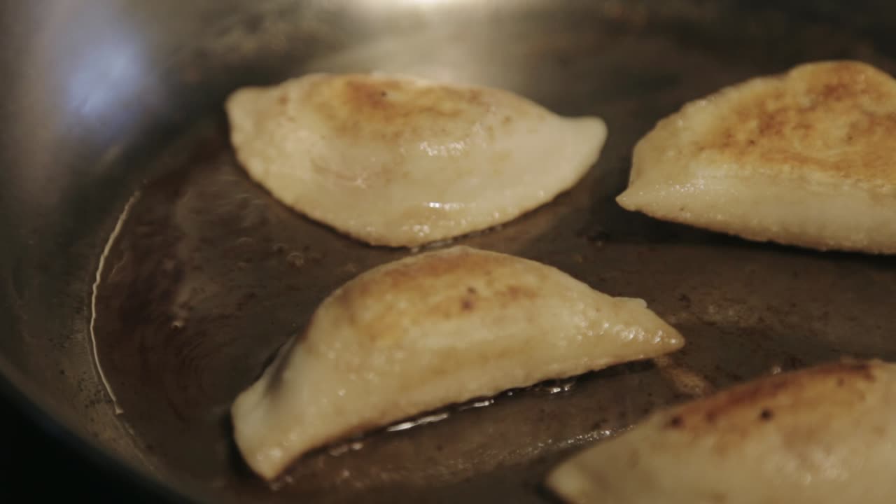 Canada - Frying Four Dumplings In A Stainless Pan With Cooking Oil - Closeup Shot