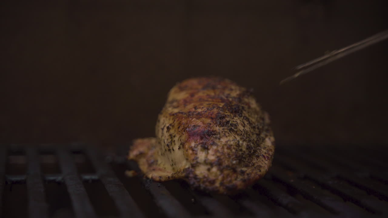 A poker moving a roasted chicken breast around on a grill. Close up