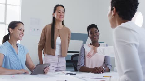 Biracial-businesswoman-shaking-hands-of-smiling-diverse-female-business-colleagues-in-office