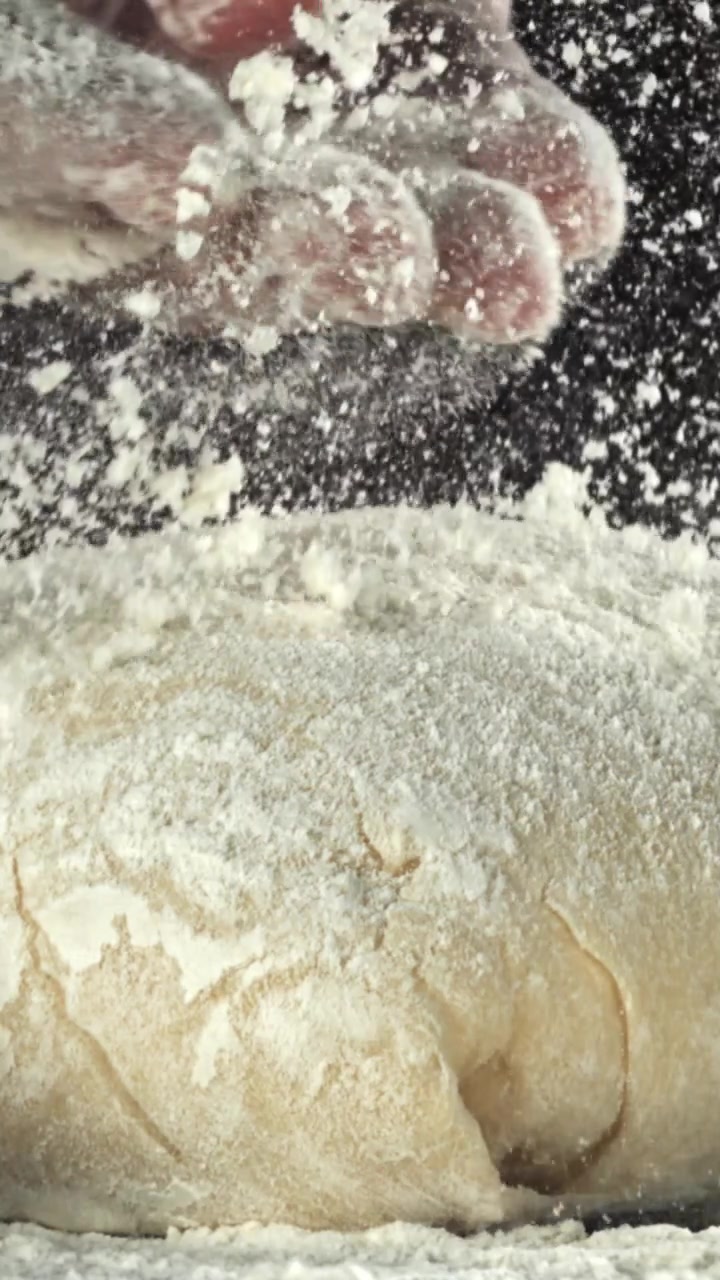 Close-up de mão polvilhando farinha sobre massa fresca em câmera lenta