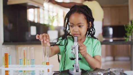 Focused-african-american-daughter-using-microscope,-doing-science-experiments-at-home