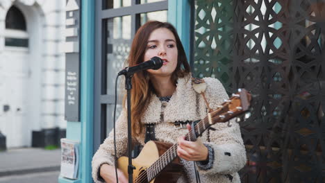 female musician busking playing acoustic guitar and singing outdoors in street