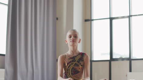 portrait of a young rhythmic gymnast sitting on floor in a studio and smiling at camera