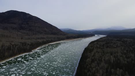 icy liard river in canada at winter with cloudy forest, aerial drone