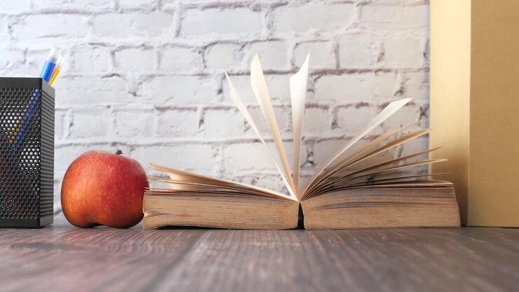 Libro aperto, mela e matite su un tavolo di legno