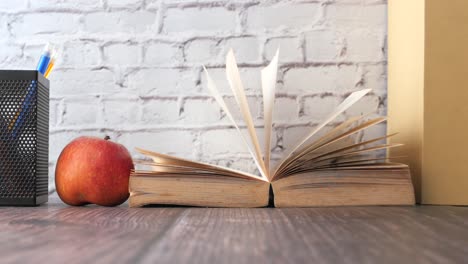 libro abierto, manzana y lápices en una mesa de madera