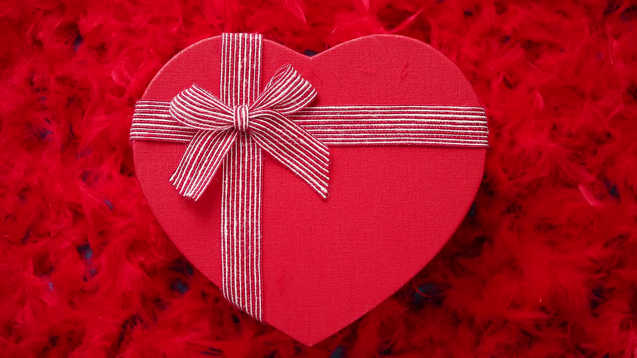 regalo in scatola a forma di cuore posto su sfondo di piume rosse