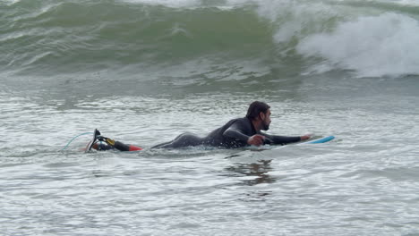 Hombre-Deportivo-En-Traje-De-Neopreno-Con-Pierna-Artificial-Acostado-En-La-Tabla-De-Surf-Y-Nadando-En-El-Océano-Cuando-Una-Ola-Lo-Cubre-2