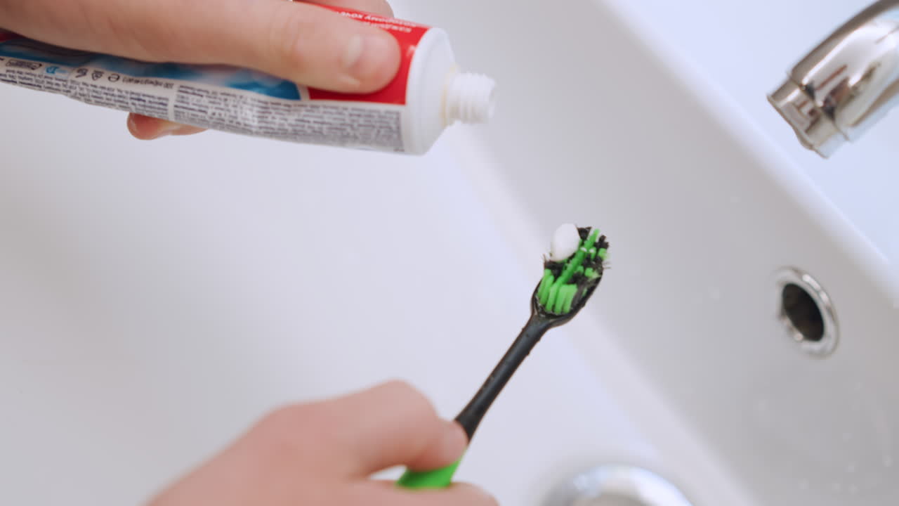 Gentle hands of grandma applying paste onto brush near sink calm bedtime routine careful measured squeeze green bristles white paste soft bathroom lighting warm caregiving moment comfort and support