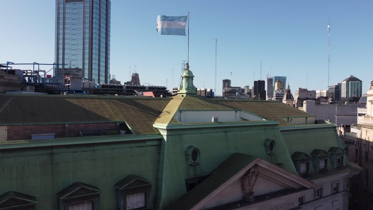bandera argentina ondeando en el techo del edificio del banco de la nación argentina con rascacielos en segundo plano