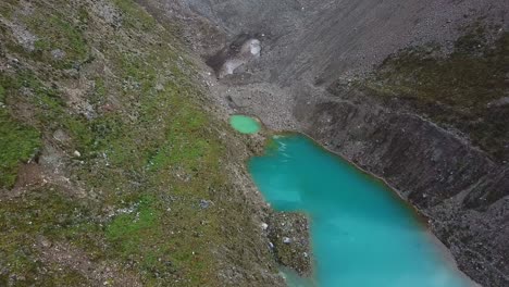 Aerial,-drone-shot-overlooking-a-reflecting,-emerald-water-of-lake-Humantay,-Andes-mountains,-overcast-day,-in-Peru,-South-America